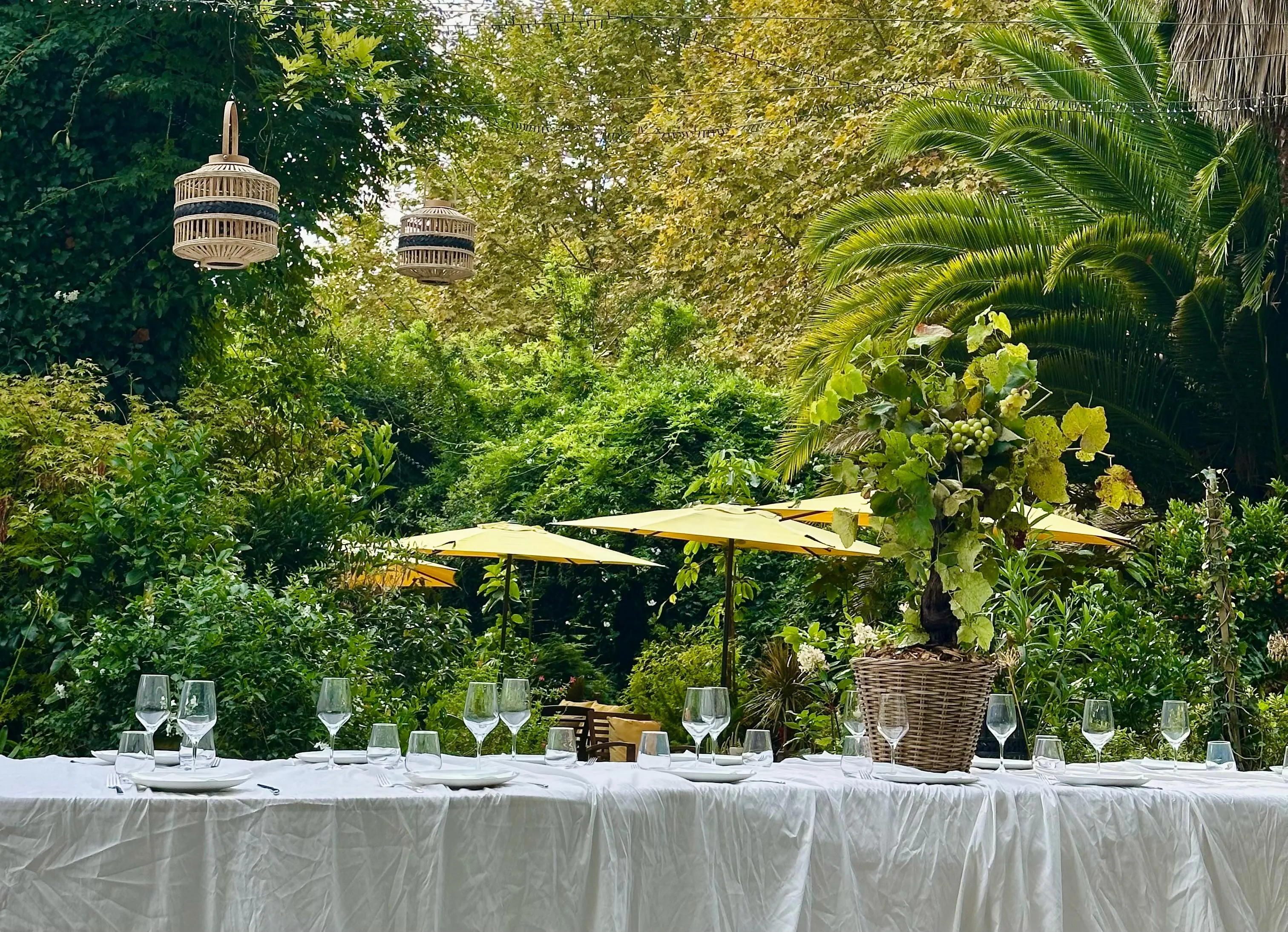 Grande tablée dressée dans un jardin, verres à vin et parasols